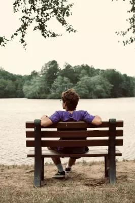 Un hombre de espaldas sentado en un banco a orillas de un lago