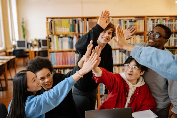 Cinco adolescentes chocan las manos en una biblioteca
